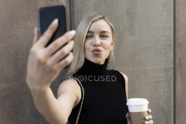 Porträt einer blonden Frau mit Kaffee-to-go-Selfie mit Smartphone — Stockfoto