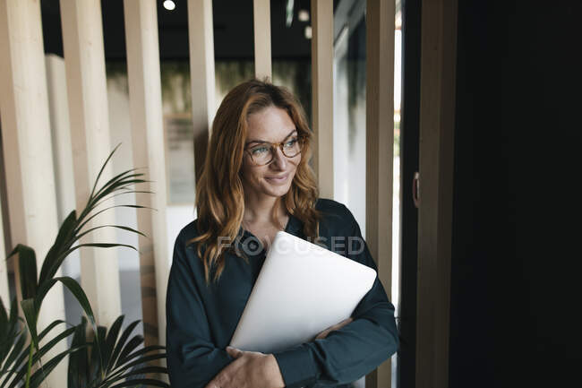 Усміхнена бізнес-жінка тримає ноутбук дивлячись в сторону — стокове фото