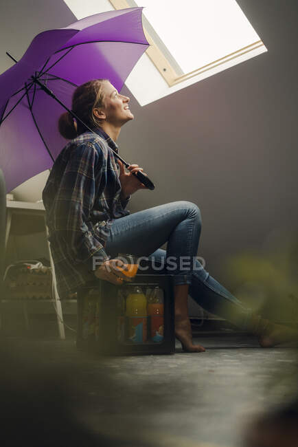Lächelnde junge Frau mit Regenschirm, die aus dem Fenster schaut — Stockfoto