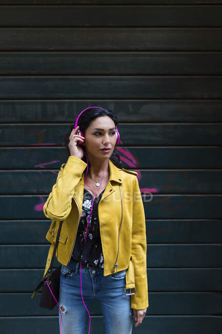Retrato de mulher jovem com fones de ouvido rosa, usando jaqueta de couro amarelo — Fotografia de Stock