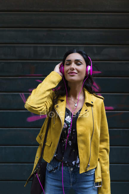 Retrato de mulher jovem com fones de ouvido brancos, usando jaqueta de couro preto — Fotografia de Stock