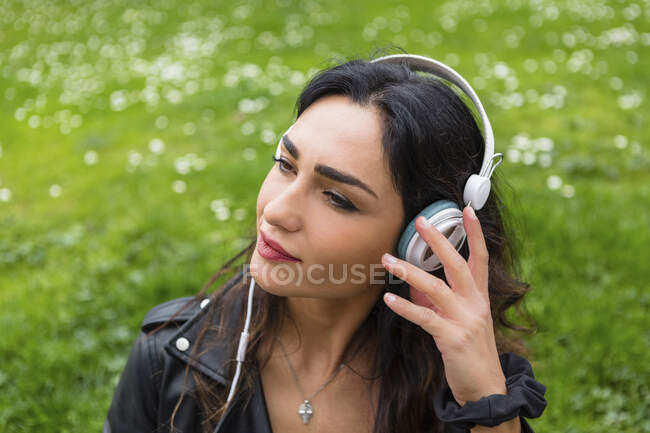Retrato de mulher jovem com fones de ouvido brancos, usando jaqueta de couro preto — Fotografia de Stock
