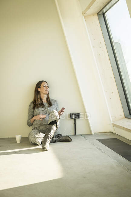Pregnant woman drinking tea, sitting on floor of her new home — Stock Photo