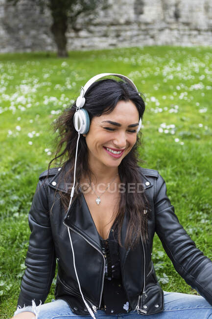 Retrato de mulher jovem com fones de ouvido brancos, usando jaqueta de couro preto — Fotografia de Stock