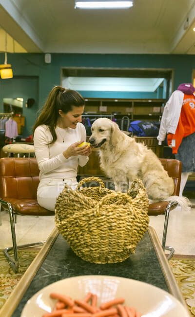 Smiling woman with dog sitting on chair in a vintage boutique — Stock Photo
