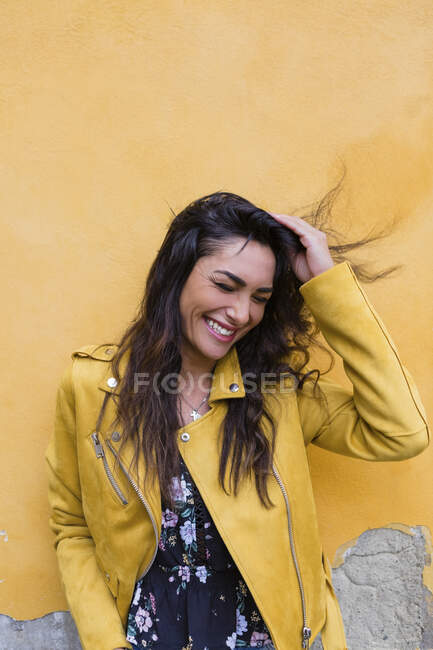 Retrato de jovem mulher rindo usando jaqueta de couro amarelo, mão no cabelo — Fotografia de Stock