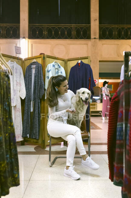 Smiling woman with dog sitting on chair in a vintage boutique — Stock Photo
