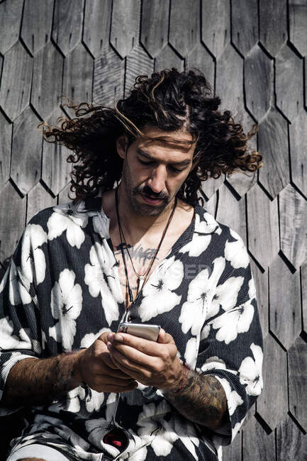 Портрет человека с татуировкой в гавайской рубашке, смотрящего на сотовый телефон — стоковое фото