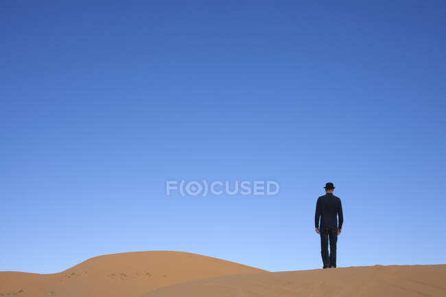 Marrocos, Merzouga, Erg Chebbi, visão traseira do homem usando um chapéu de jogador em pé na duna do deserto — Fotografia de Stock