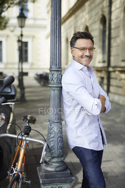 Portrait d'homme d'affaires souriant avec vélo appuyé contre le lampadaire dans la ville — Photo de stock