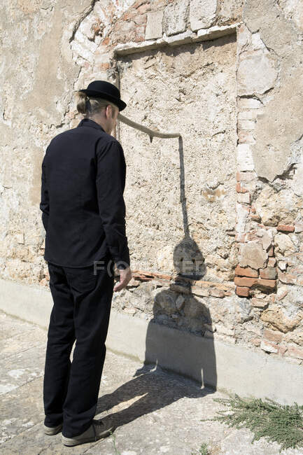 Homem usando um chapéu de jogador equilibrando um pau em uma parede de pedra — Fotografia de Stock