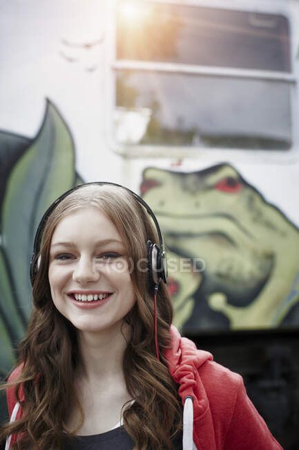 Портрет счастливой девочки-подростка в наушниках в раскрашенном вагоне — стоковое фото