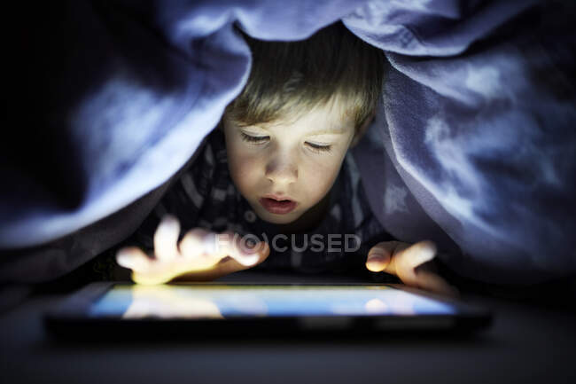 Niño jugando en secreto con su tableta digital, manta oculta uunder - foto de stock