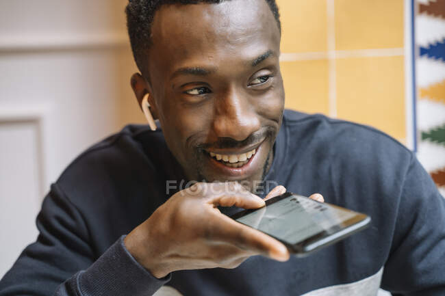 Retrato de un joven sonriente con auriculares inalámbricos en el teléfono - foto de stock