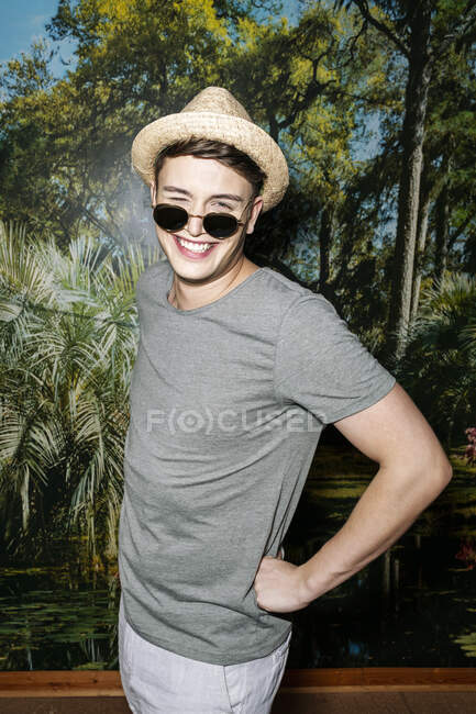 Junger Mann mit Hut und Sonnenbrille steht vor Fototapete und lacht — Stockfoto