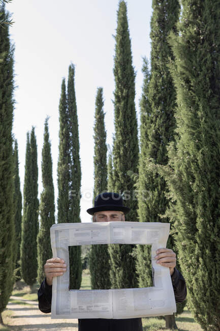 Italy, Tuscany, invisible man surrounded by cypresses reading newspaper with a hole — Stock Photo