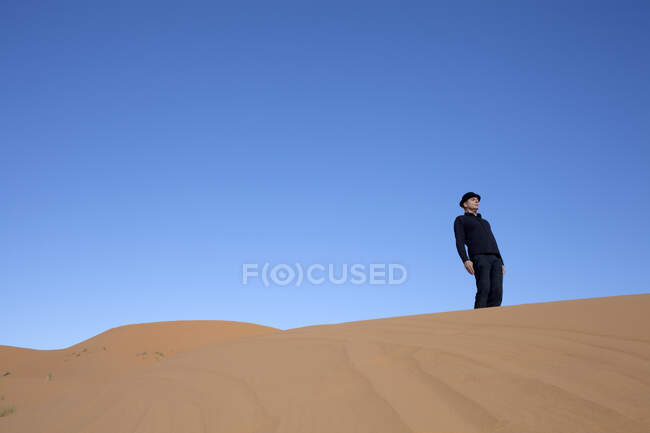 Marrocos, Merzouga, Erg Chebbi, homem usando um chapéu de jogador de pé torto na duna do deserto — Fotografia de Stock