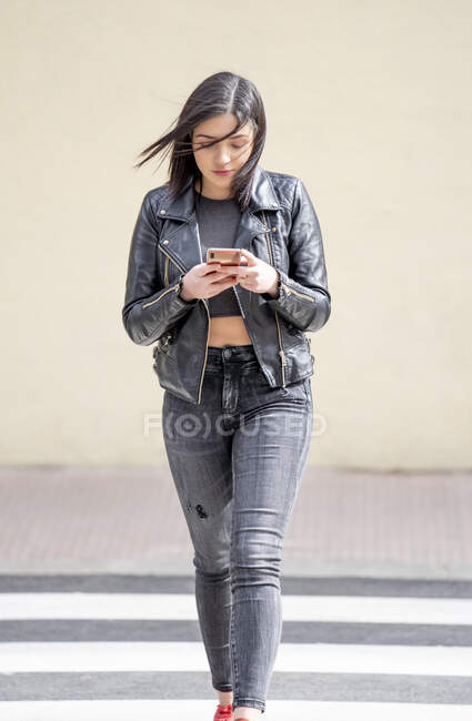 Young woman crossing the pedestrian crossing and using mobile phone — Stock Photo