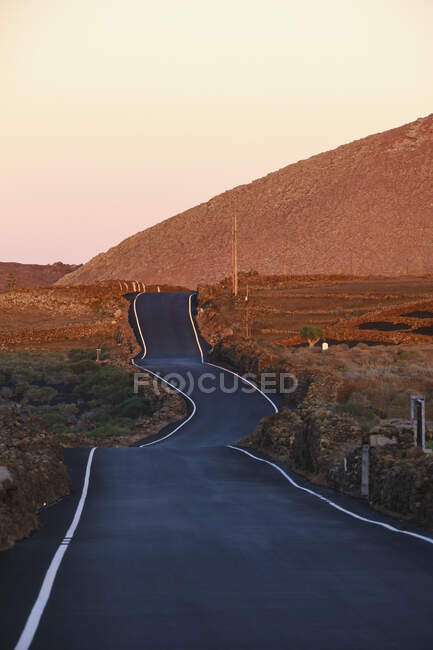España, Islas Canarias, Lanzarote, Tinajo, carretera rural al atardecer - foto de stock