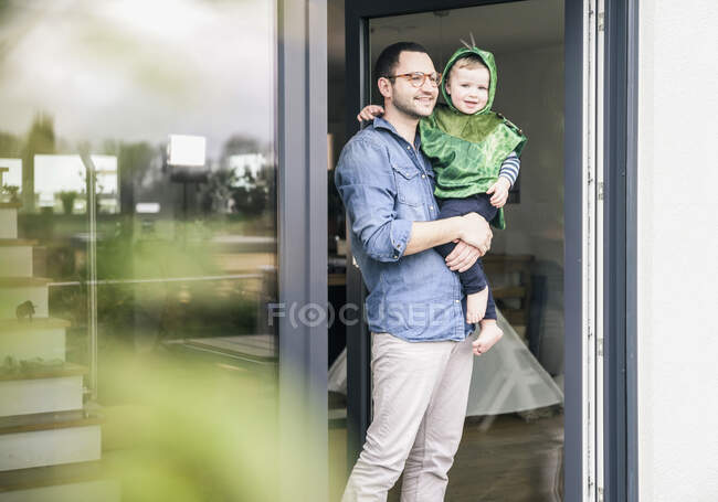 Pai carregando filho em um traje na porta do terraço em casa — Fotografia de Stock