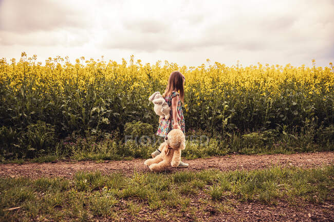 Menina andando sozinha com pelúcia e mochila em um caminho de campo — Fotografia de Stock