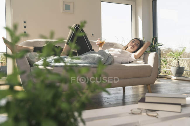Mujer joven y relajada tumbada en el sofá con una bebida - foto de stock