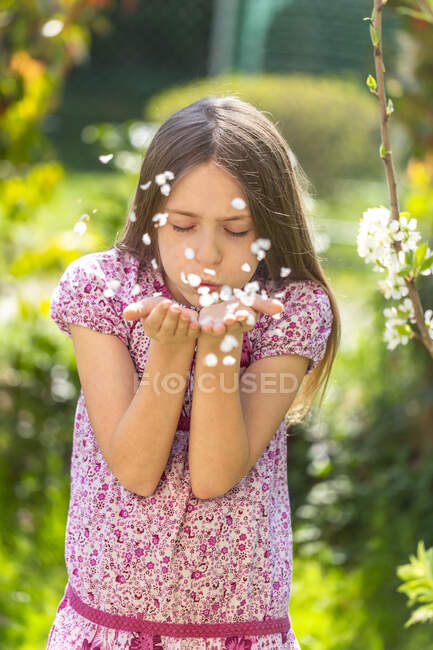 Ritratto di ragazza che soffia petali in giardino — Foto stock