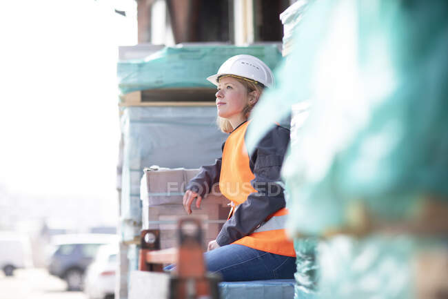 Woman wearing reflective vest and hard hat sitting on building material — Stock Photo