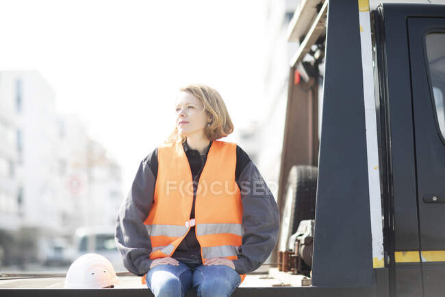 Mujer con chaleco reflectante sentado en la plataforma del camión - foto de stock
