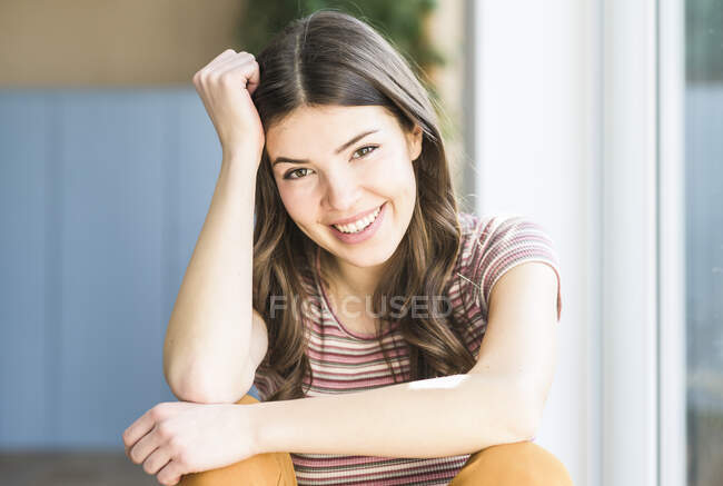 Ritratto di giovane donna sorridente seduta alla finestra di casa — Foto stock