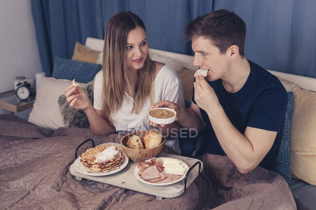 Young couple having breakfast in bed — Stock Photo