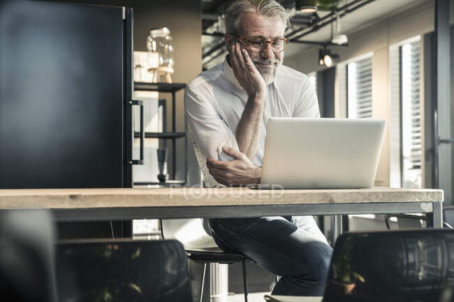 Sorridente uomo d'affari maturo guardando computer portatile in ufficio — Foto stock