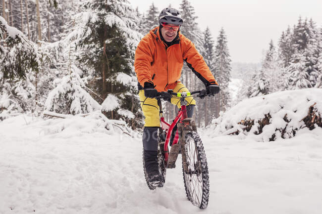 Ritratto di uomo felice in sella alla mountainbike sul sentiero nella foresta invernale — Foto stock