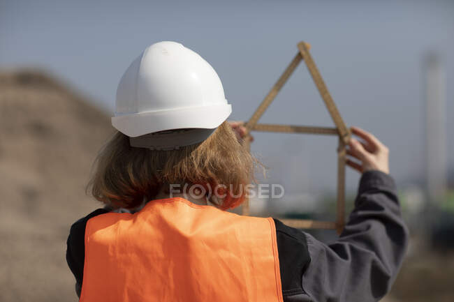 Vista posteriore della donna che indossa giubbotto riflettente e cappello rigido regola tasca in forma di una casa — Foto stock