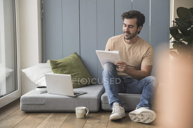 Молодой человек сидит на матрасе, пользуется ноутбуком, делает заметки — стоковое фото