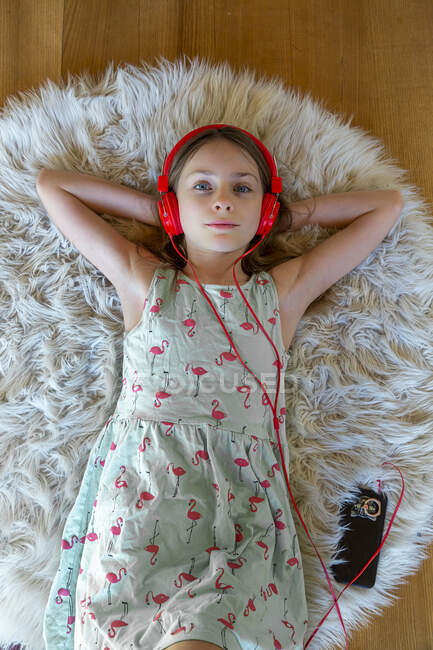 Girl lying on carpet at home listening to music with headphones and smartphone — Stock Photo