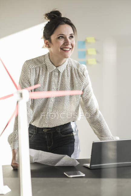 Smiling businesswoman with wind turbine model and laptop on desk in office — Stock Photo
