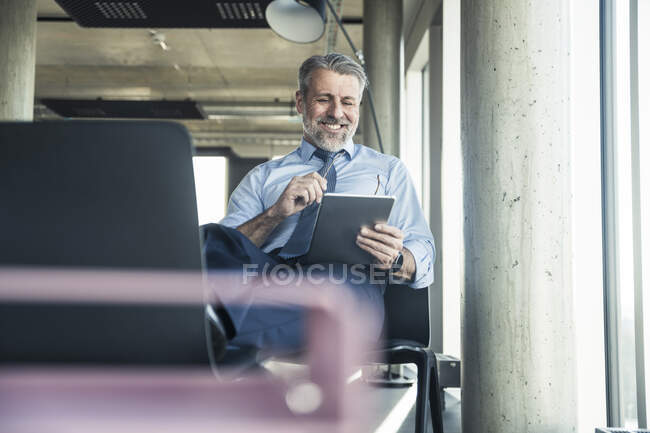 Усміхнений зрілий бізнесмен сидить на стільці за допомогою планшета — стокове фото