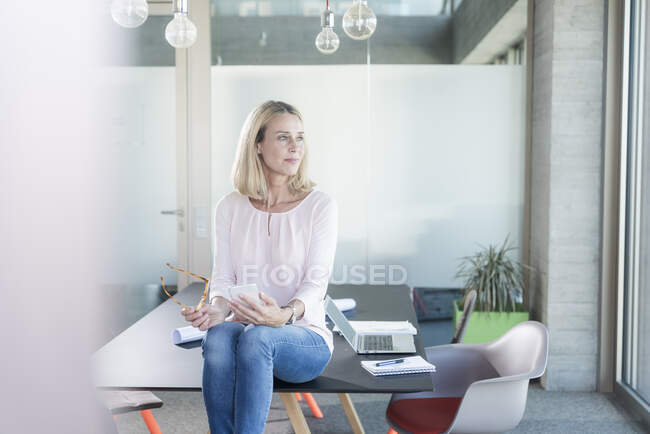 Femme d'affaires assis sur le bureau dans le bureau regardant latéralement — Photo de stock