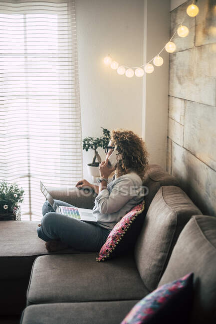 Frau zu Hause mit Laptop und Handy auf Couch — Stockfoto