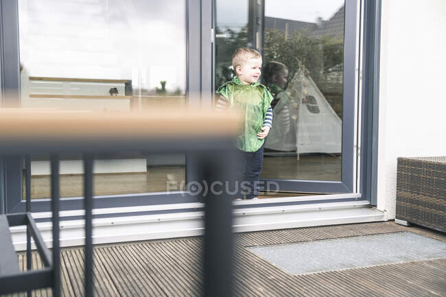 Щасливий хлопчик у костюмі, що стоїть біля дверей тераси. — стокове фото