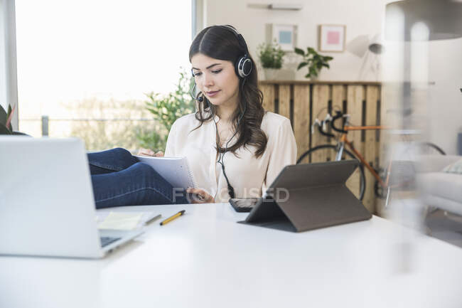 Молодая женщина сидит дома за столом в наушниках — стоковое фото