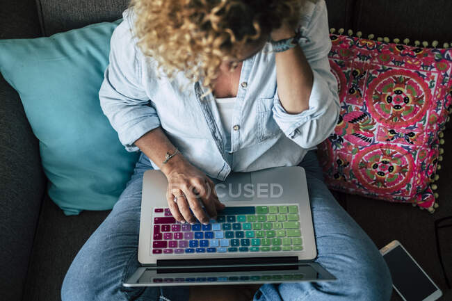 Donna che utilizza laptop con tastiera multicolore sul divano di casa — Foto stock