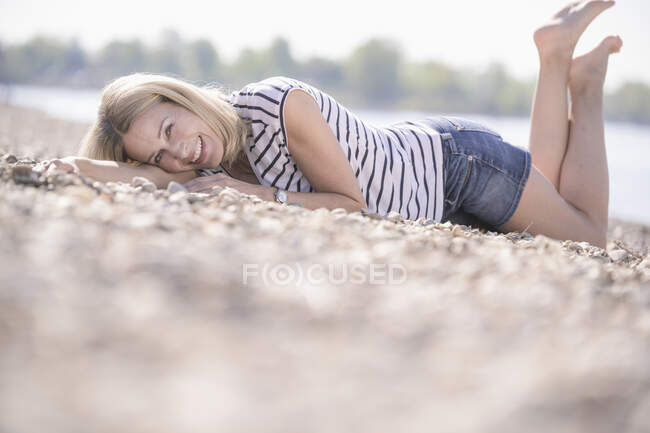 Happy mature woman lying on pebbles at the riverside — Stock Photo