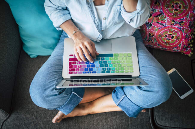 Donna che utilizza laptop con tastiera multicolore sul divano di casa — Foto stock