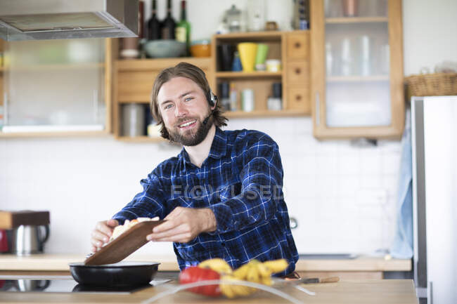 Young man with beard and plaid shirt, and headset cooking vegetables in kitchen — Stock Photo
