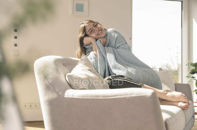 Mujer joven feliz con manta de lana en el sofá - foto de stock