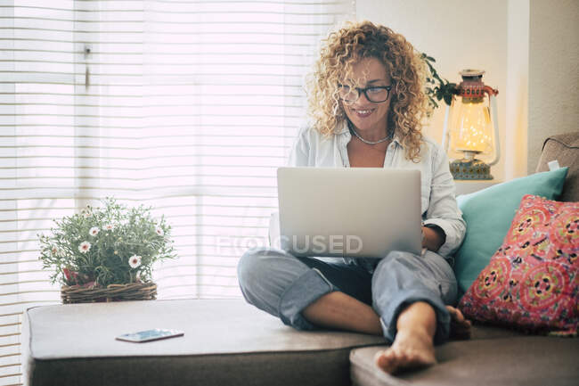 Усміхнена жінка використовує ноутбук на дивані. — стокове фото