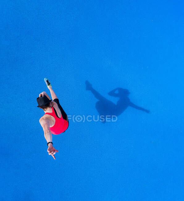 Jeune femme sautante et son ombre sur fond bleu, vue de dessus — Photo de stock