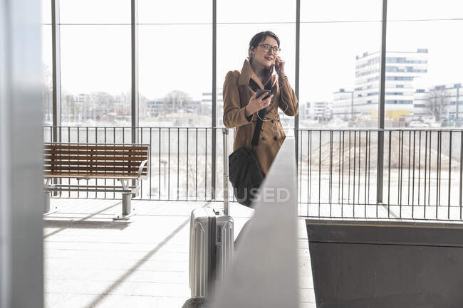 Mujer de negocios con equipaje y teléfono celular aplicando auriculares — Stock Photo